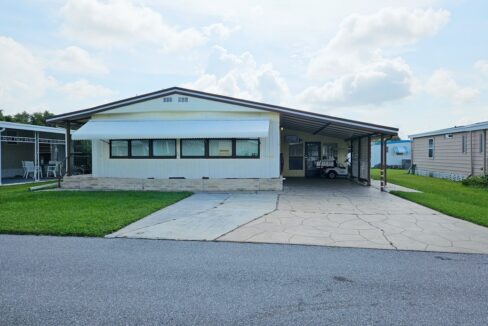 Outside view of yellow double-wide home with brown trim, carport and wide driveway. Ready. Set. Relax!
