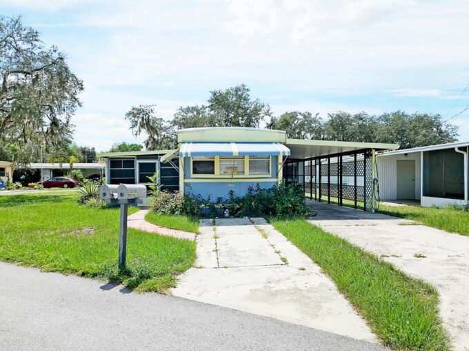 Quiet Getaway: single-wide home, blue and yellow with 2 driveways, one leading to a large attached carport, lanai attached to opposite side of home at 62 Dale Drive