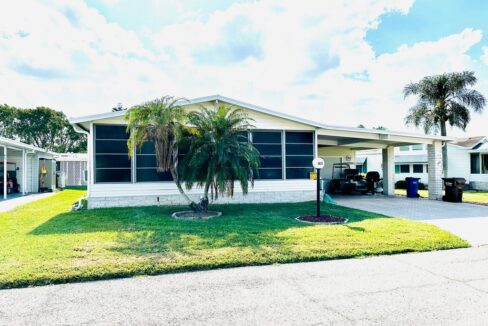 4613 Duffer PL, Lakeland, FL, a white Palm Harbor double-wide with endless possibilities. Deco driveway and carport, screened windows across front of home, palm tree in well-landscaped yard.