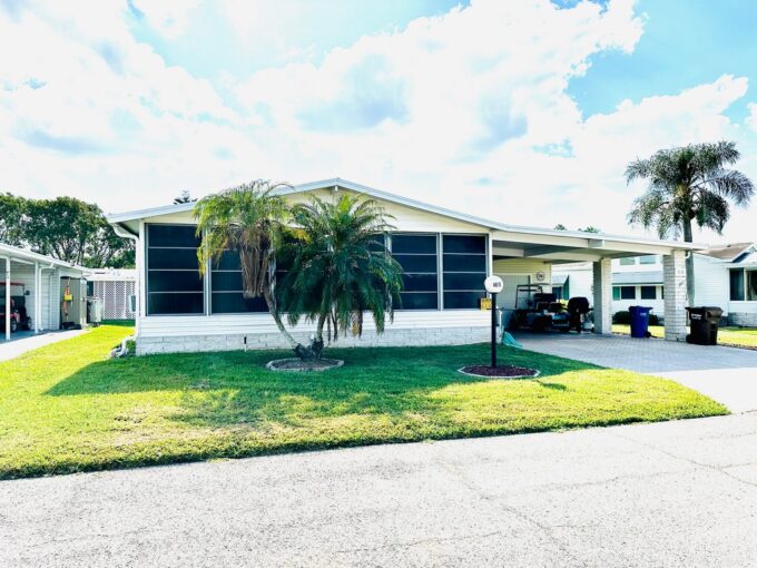 4613 Duffer PL, Lakeland, FL, a white Palm Harbor double-wide with endless possibilities. Deco driveway and carport, screened windows across front of home, palm tree in well-landscaped yard.