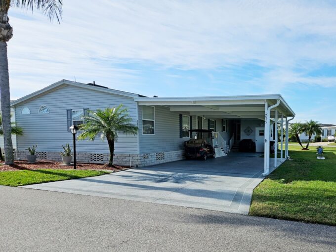 Easy to Love home at 235 Monterey Cypress BLVD, Winter Haven, IN. White Vinyl 2007 TIMB double-wide with deco driveway to wide carport covering entrance to home