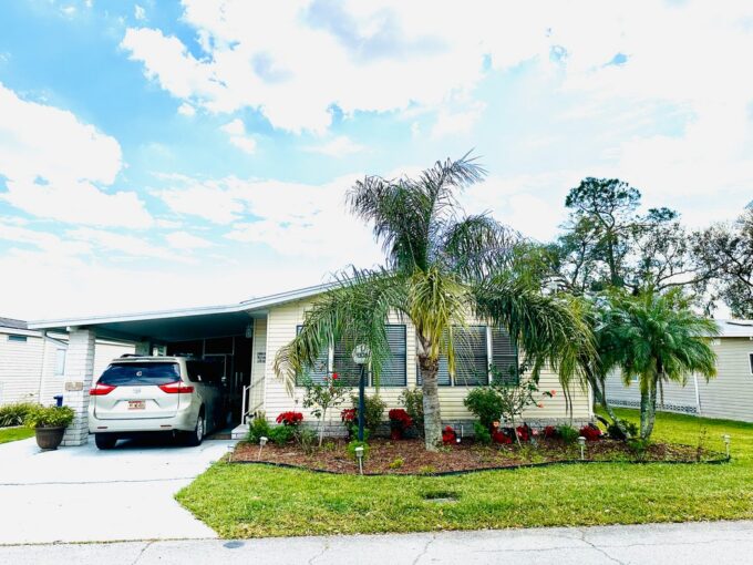This great home at 1308 Deverly DR, Lakeland, FL, comes with an inspiring panoramic view from the back lanai and patio. Yellow vinyl sided double-wide manufactured home with tropical landscaping and wide driveway