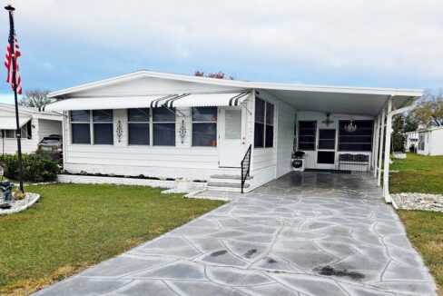 Move in ready. turnkey home at 206 Rainbow LN W, Dundee Florida. Deco driveway leads to front entrance of the double-wide white home with black and white awnings, carport and screened lanai