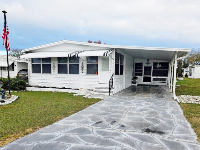 Move in ready. turnkey home at 206 Rainbow LN W, Dundee Florida. Deco driveway leads to front entrance of the double-wide white home with black and white awnings, carport and screened lanai
