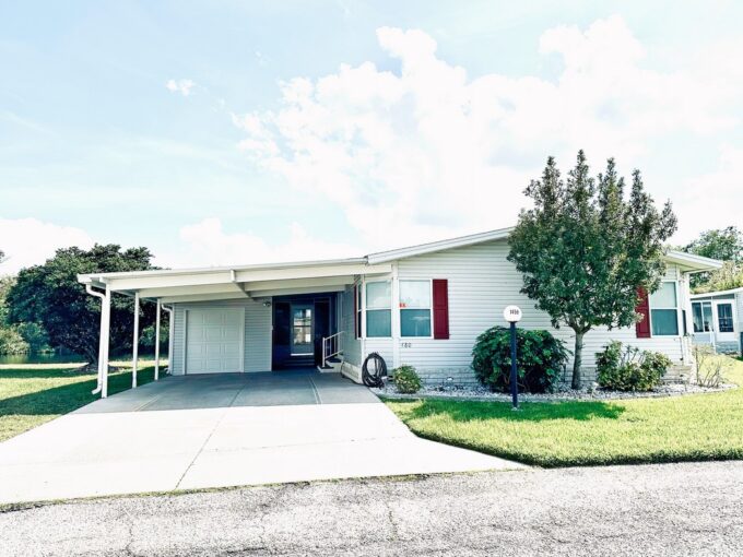 Stunning water views await at 1459 Crooked Stick Loop, Lakeland, Florida. 1992 CHAN manufactured double-wide home with light gray vinyl siding, wide deco driveway and eye-catching landscaping.
