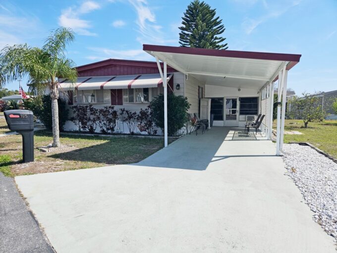 Comfortable Getaway at 195 Rainbow LN W, Dundee, FL. Wide driveway leading to covered carport which ends at a lanai. Awnings on front of home.