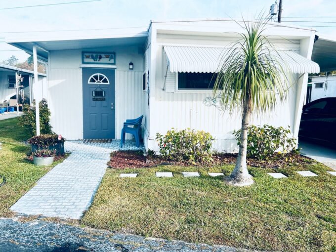 35 CC St, Lakeland Florida: IMMACULATE FLORIDA RETREAT. White singlewide with tropical landscaping and blue door at entrance.