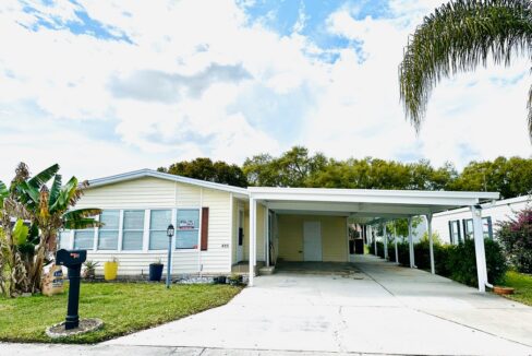Delightful tropical oasis...your home at 415 McElwee DR, Auburndale, Florida. Beautiful yellow vinyl home with a bank of windows across the front and a double-wide driveway leading to a large carport.