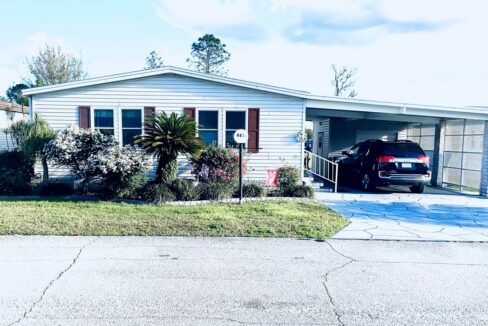 Remodeled 1991 Palm Harbor home at 4631 Cedarbrook Way, Lakeland, FL, offers Golf Views for Serene Senior Living. Gray Vinyl Siding with deco driveway and carport, tropical landscaping
