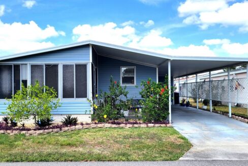 Charming Home featuring an upgraded kitchen and Nestled in Enchanting Community at 2233 Parrot Place, Lake Wales, Florida. Double-Wide manufactured home on with blue siding and white trim, front-facing lanai, landscaped yard and entrance, driveway to carport