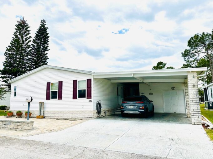 This treasured home is one of a kind at 4312 Dirkshire Loop is a triple-wide home with lanai. White Vinyl siding with Maroon Shutters, double-wide driveway and carport with golf cart garage. Large front patio area.