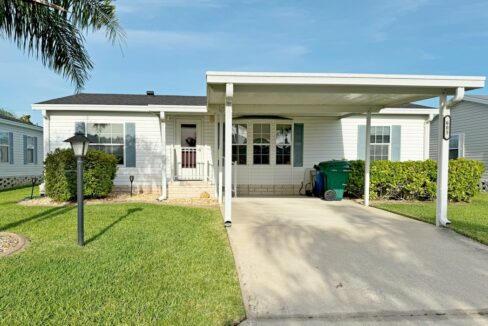 Special Sunshine Retreat at 605 Yellow Cypress Lane in the Cypress Creek Village, Winter Haven, Florida. Double-wide manufactured home with driveway leading to carport on front of white vinyl-sided home