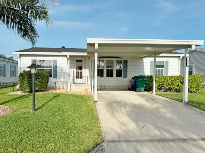 Special Sunshine Retreat at 605 Yellow Cypress Lane in the Cypress Creek Village, Winter Haven, Florida. Double-wide manufactured home with driveway leading to carport on front of white vinyl-sided home