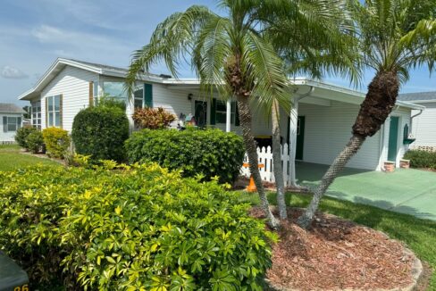 Tastefully Landscaped Yard at 921 La Quinta BLVD, Winter Haven, FL, in a golf community. Double-Wide Manufactured home with White Vinyl Siding and Green Deco Driveway and shutters.