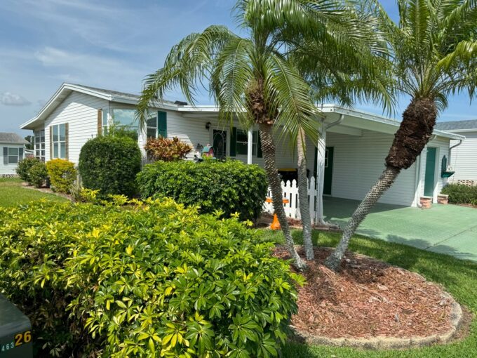 Tastefully Landscaped Yard at 921 La Quinta BLVD, Winter Haven, FL, in a golf community. Double-Wide Manufactured home with White Vinyl Siding and Green Deco Driveway and shutters.