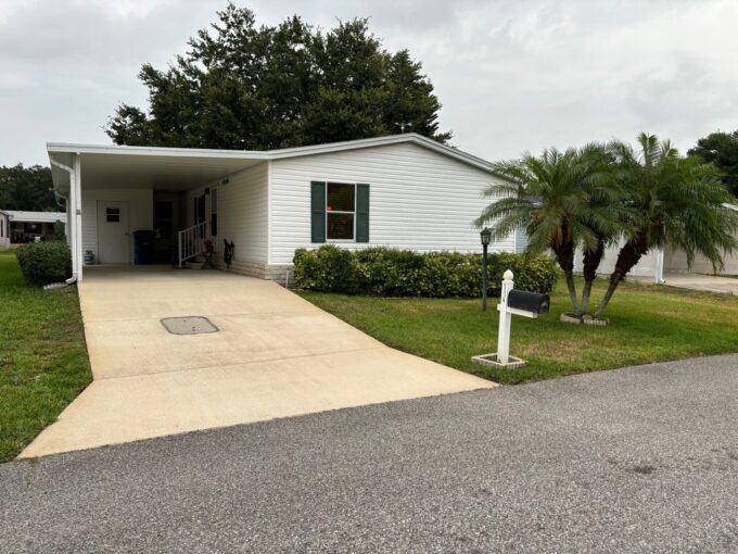 114 Winterdale DR Lot 199 Kings Pointe Community in Lake Alfred, FL. White vinyl siding with green shutters. carport, gutters, private driveway and curb side mail.