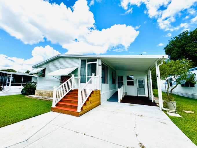 246 Greenhaven Land W in Dundee. 1993 Palm Harbor with 1824 sq ft. Gray and white exterior colors, private driveway, carport, gutters with access ramp.