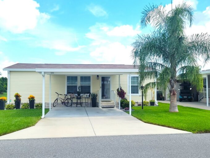 1202 Cypress Vine Lot #356 in Winter Haven. Beautiful 2021 model with nice landscaping, yellow vinyl siding, carport, gutters, private driveway.