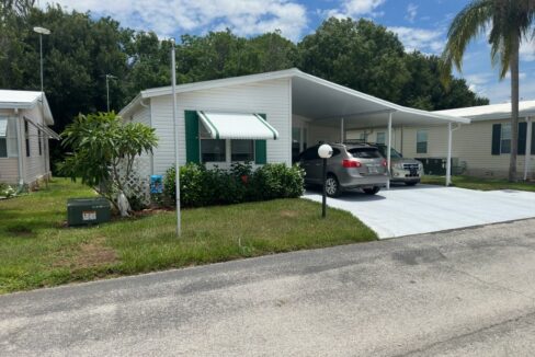 311 Maple Crest Drive located in The Landings at Lake Henry in Haines City. White exterior with green trim, double carport, oversized driveway. Awning on the front window.