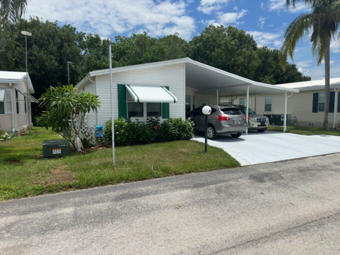 311 Maple Crest Drive located in The Landings at Lake Henry in Haines City. White exterior with green trim, double carport, oversized driveway. Awning on the front window.