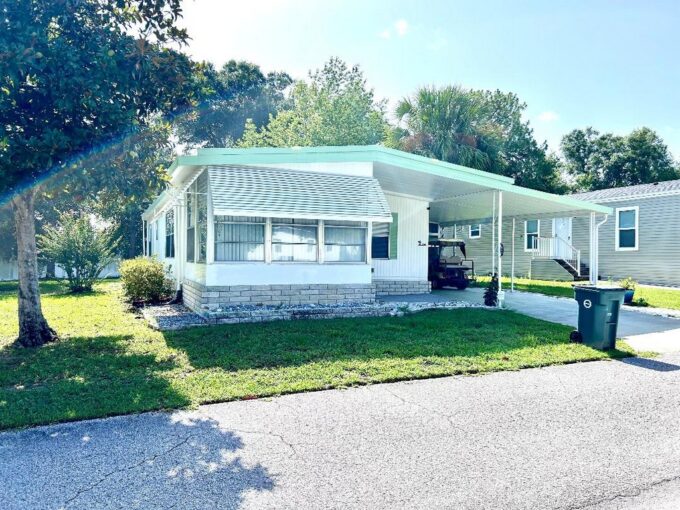 3150 NE 36th Ave #390 in Ocala located in Villas at Spanish Oaks. Brick skirting, white siding with green accents, carport, gutters, private driveway.