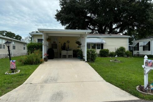 408 Gulf Stream in Kings Pointe, Lake Alfred. Exterior of this duble wide is yellow with white trim. Includes carport, private driveway, curb side mail delivery, gutters, awning and mature landscaping.