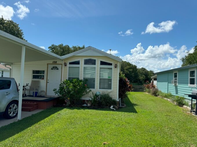 View 2 - Bay windows, yellow vinyl siding, carport, private driveway, nice landscaping.