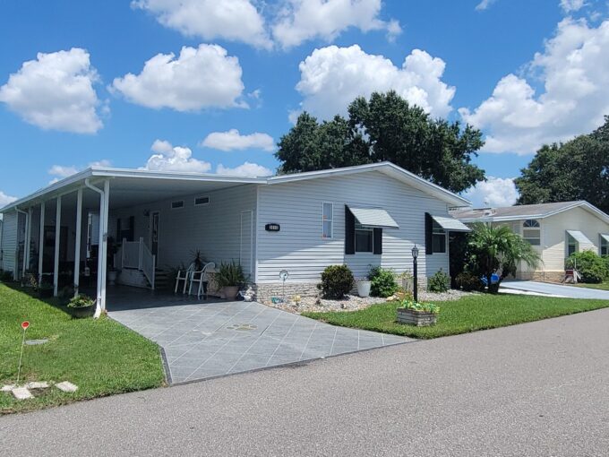 Light gray siding, awnings, carport, private deco driveway, gutters, nice, landscaped yard, wide community roads.