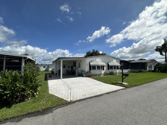 View 2 - double wide with white vinyl with black trim, awnings, oversized private driveway, carport, gutters, with 12 x 12 lanai, curb side mail delivery.