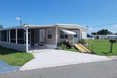 View 2 - Tan vinyl siding with awnings, screened lanai, storage shed, gutters, private drive, waterfront, curb side mail delivery.