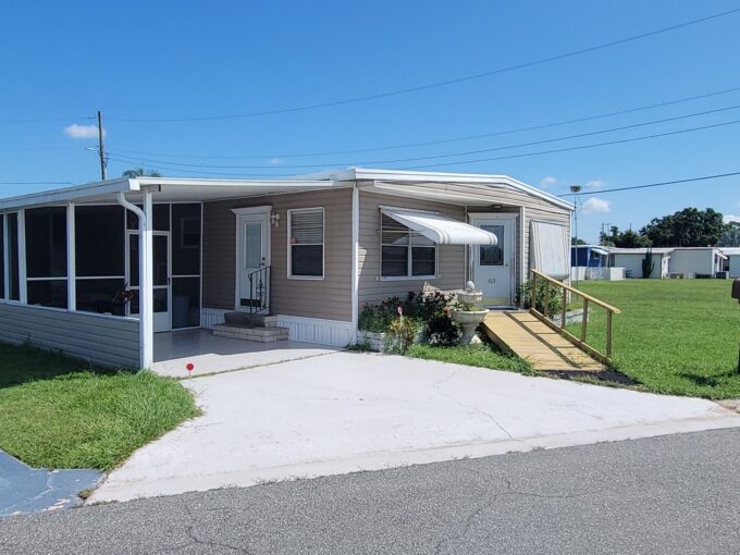 View 2 - Tan vinyl siding with awnings, screened lanai, storage shed, gutters, private drive, waterfront, curb side mail delivery.