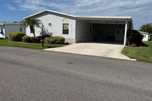 Gray vinyl siding with white shutters, carport, gutters, landscaped yard with cement curbing, private driveway, oversized shed that is a golf cart garage with workbench.