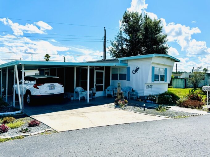 Single wide with white vinyl siding, teal trim,11x17 Lanai and 2 8x10 sheds, carport, private driveway, curb side mail delivery, beautiful landscaping