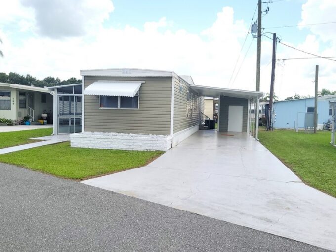 Tan single wide that has been remodeled. With screened lanai, private driveway, carport, gutters, awnings and storage shed.