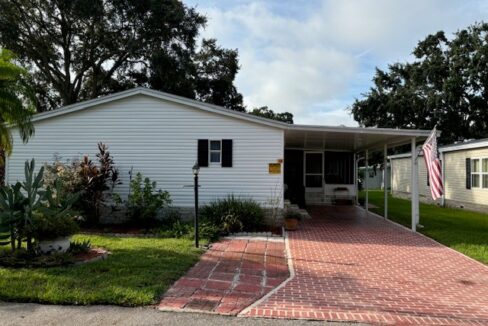 305 Winter Garden in Kings Pointe community located in Lake Alfred. White vinyl siding with a private deco driveway, carport, screened lanai, gutters, yard lamp.