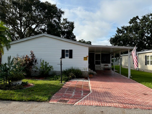 305 Winter Garden in Kings Pointe community located in Lake Alfred. White vinyl siding with a private deco driveway, carport, screened lanai, gutters, yard lamp.