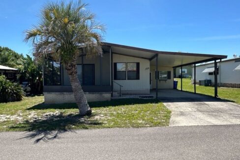 189 Edelweiss has tan siding with brown trim, private driveway, screened in lanai in the front of the home, carport with gutters, storage shed with workshop.