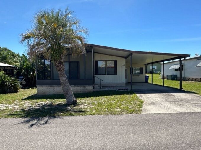 189 Edelweiss has tan siding with brown trim, private driveway, screened in lanai in the front of the home, carport with gutters, storage shed with workshop.