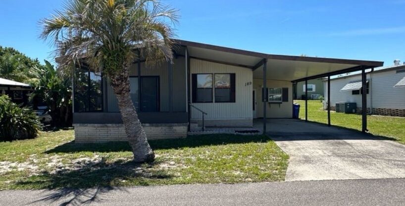 189 Edelweiss has tan siding with brown trim, private driveway, screened in lanai in the front of the home, carport with gutters, storage shed with workshop.