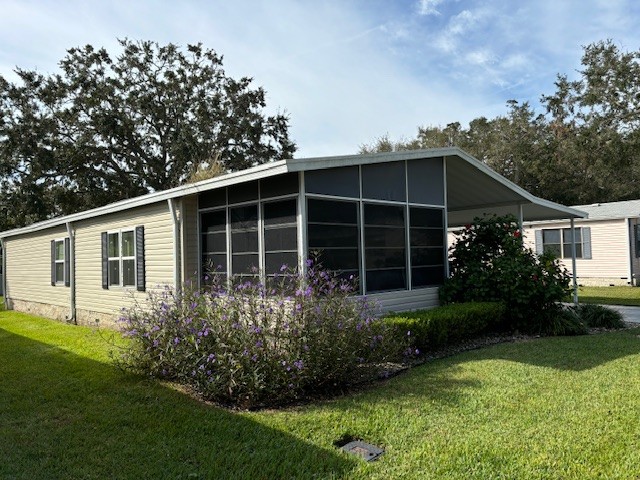 Tan vinyl siding with white trim, front lanai, private driveway, carport with gutters, storage shed at the end of the driveway. Manicured lawn.