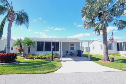 Vinyl siding in light blue with white trim, carport, front lanai, private driveway, gutters, manicured yard, storage shed in back of home.