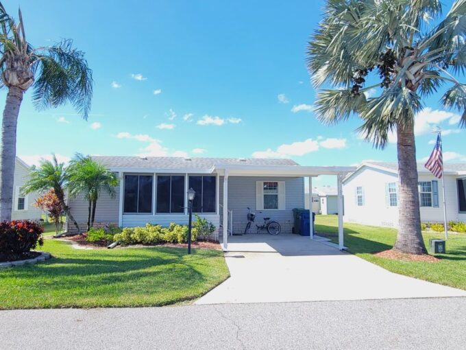 Vinyl siding in light blue with white trim, carport, front lanai, private driveway, gutters, manicured yard, storage shed in back of home.