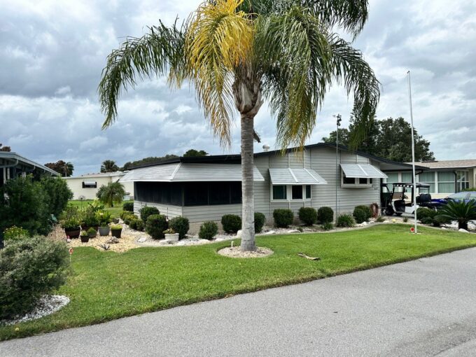 Grey siding with black trim, awnings, carport, private driveway, nice landscaping, glass lanai, screened lanai, gutters, shed that is large enough to be a workshop.