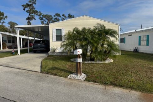 Yellow double wide with curb side mail delivery, private driveway, carport, gutters, storage shed, mature landscaping.