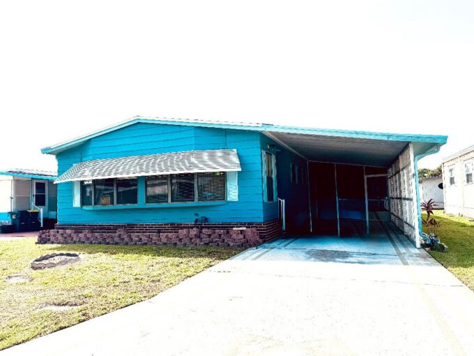 blue home with awnings, that has 2 bedrooms and 2 bathrooms, private driveway, carport, screened lanai, storage shed in a 55+ community.